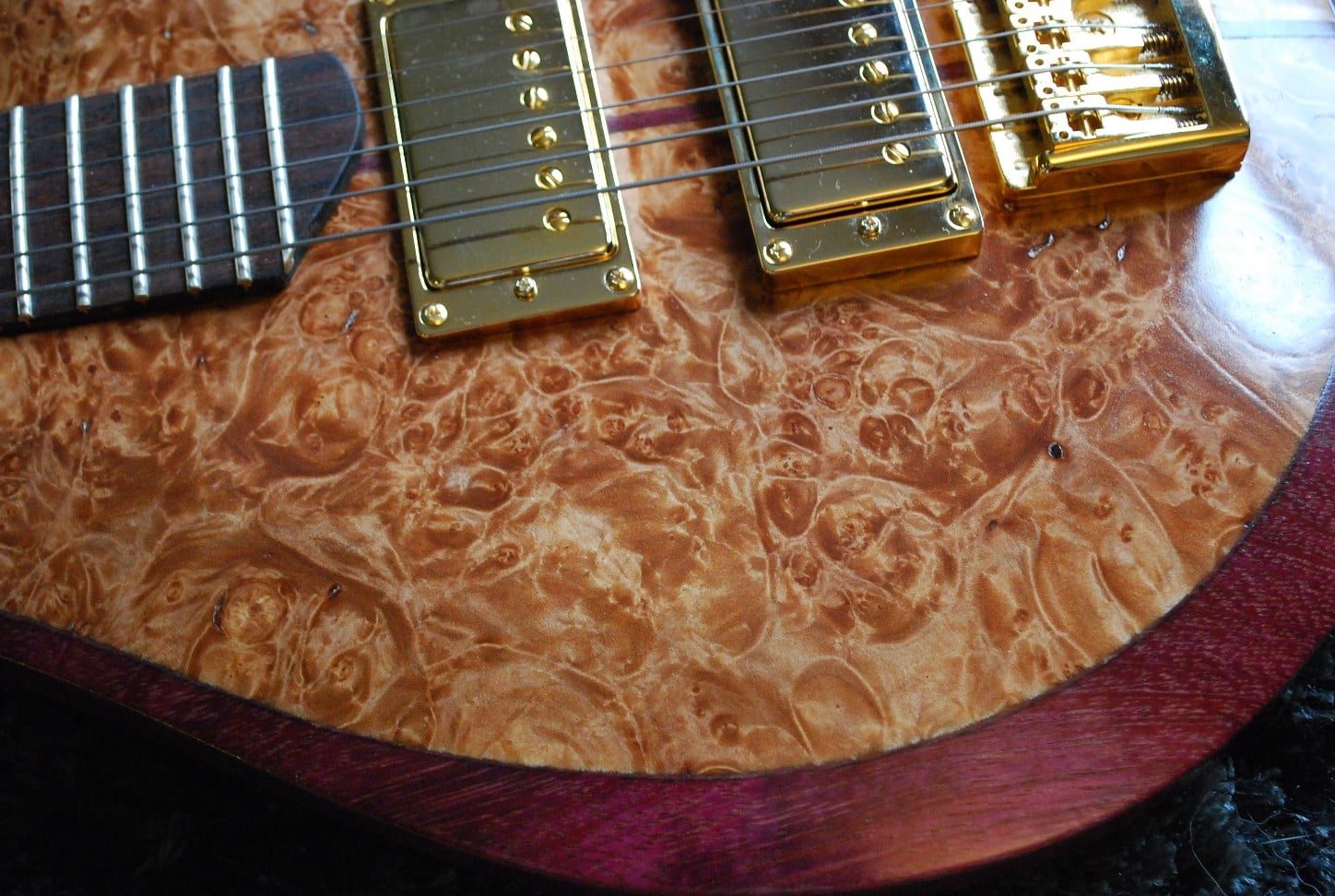 Close-up of a burl wood guitar top with gold pickups